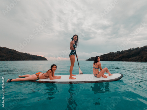 group of asian woman friends playing stand up paddle board in the sea when sunset. © Vajirawich