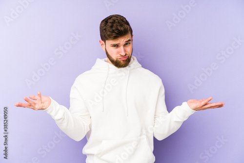 Young caucasian man isolated on purple background doubting and shrugging shoulders in questioning gesture.