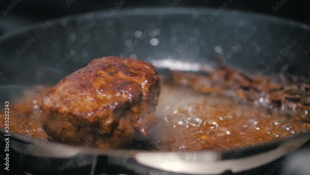Slow motion of the chef moving a frying pan with a steak inside. Close-up of the meat steak frying in a brown sauce