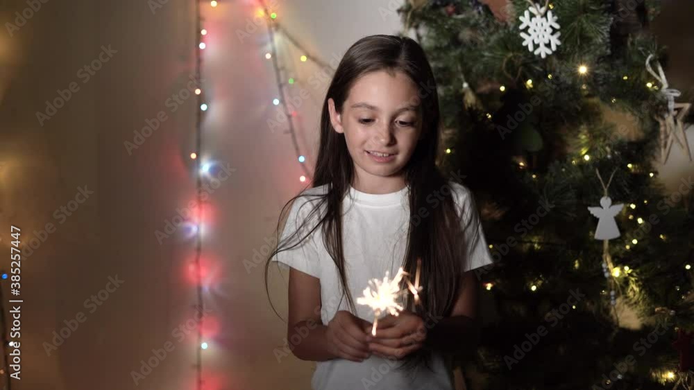 A little girl stands near a Christmas tree holding burning sparklers in her hands A little girl stands near a Christmas tree holding burning sparklers in her hands