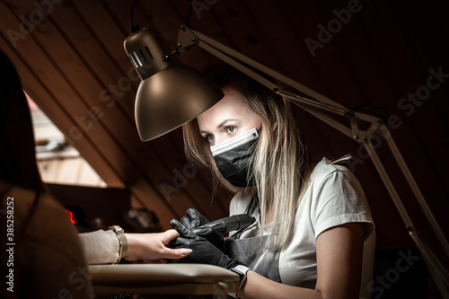 Closeup shot of a woman in a nail salon receiving a manicure by a beautician with nail file. Woman in protective medical mask and manicurist © Надія Коваль