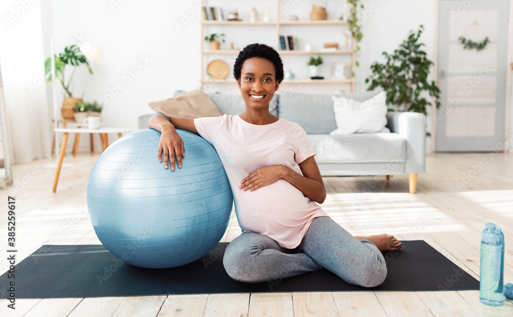 Exercising during pregnancy. Full length portrait of happy expectant woman sitting on yoga mat with fitness ball
