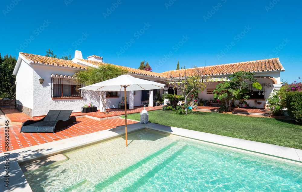 Exterior panorama of a relaxing holiday villa with a swimming pool with tanning ledge,chair pool,umbrella, grass,garden, porch and gazebo.