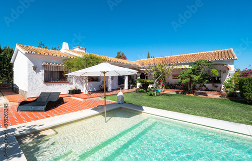 Exterior panorama of a relaxing holiday villa with a swimming pool with tanning ledge,chair pool,umbrella, grass,garden, porch and gazebo. © elroce