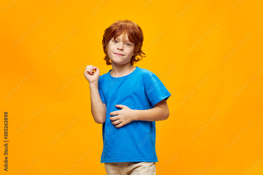 Red-haired boy in a blue t-shirt gestures with his hands smile yellow background. Red-haired boy in a blue t-shirt gestures with his hands smile yellow background.