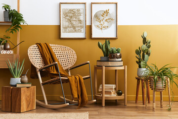 Stylish composition of living room interior with design rattan armchair, two mock up poster frames, plants, cube, palid and personal accessories in honey yellow home decor. Template.