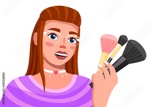 Young brown haired girl in glamour glasses talks about make-up brushes. Modern trendy girl with cosmetic accessories in hand. Woman with fashionable make-up and a choker on her neck. Blooger, streamer
