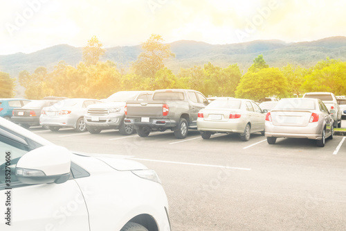 Car parked in large asphalt parking lot with trees, cloudy sky and mountain background. Outdoor parking lot with fresh ozone and green environment of travel transportation concept