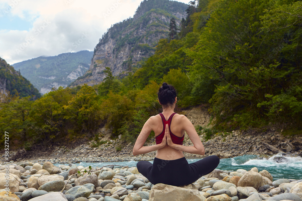 Yoga classes in nature. The concept of playing sports alone. Social exclusion. A woman does yoga on rocks, near a mountain river flows Yoga classes in nature. The concept of playing sports alone. Social exclusion. A woman does yoga on rocks, near a mountain river flows