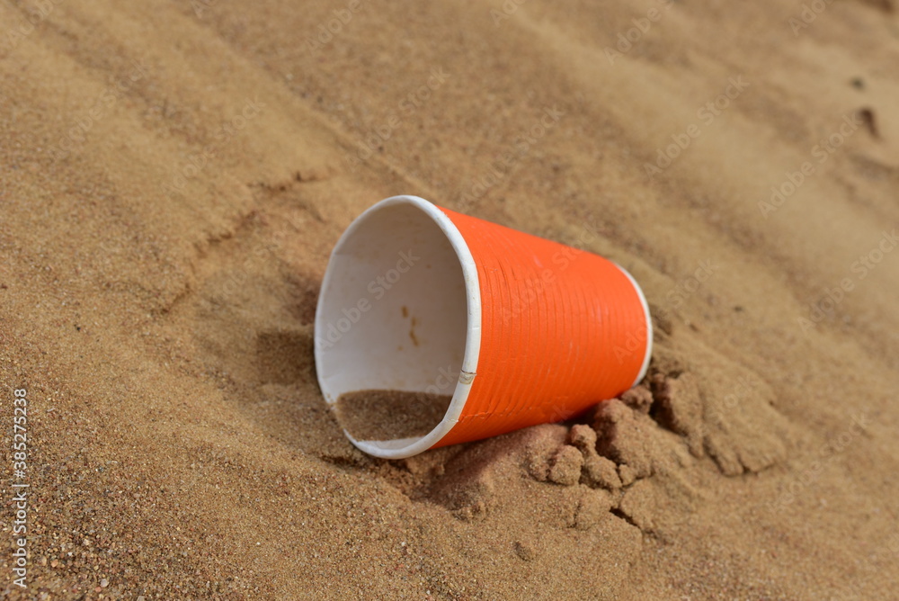 Discarded Paper coffee cup on sand at beach. Disposable coffee cup on sandy background. The problem of environmental pollution. Pile of abandoned garbage, including food waste, fast food packaging Discarded Paper coffee cup on sand at beach. Disposable coffee cup on sandy background. The problem of environmental pollution. Pile of abandoned garbage, including food waste, fast food packaging