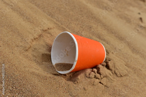 Discarded Paper coffee cup on sand at beach. Disposable coffee cup on sandy background. The problem of environmental pollution. Pile of abandoned garbage, including food waste, fast food packaging
