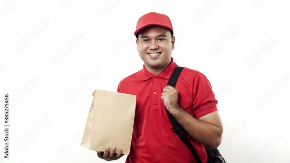 Smiling young asian delivery man in red uniform holding parcel paper bag standing on isolated white background. 4k Resolution. Smiling young asian delivery man in red uniform holding parcel paper bag standing on isolated white background. 4k Resolution.