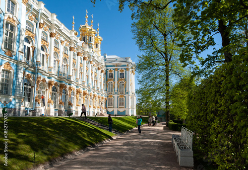 The wall of the palace with yellow stucco, a shady path with benches. Golden domes of the church against the blue sky. Tourists take pictures. Catherine Palace, (Tsarskoye Selo). 18 century