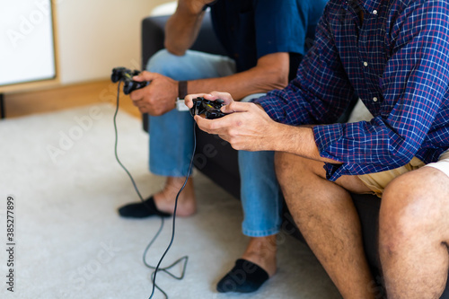 Father and son family time together at home concept. Happy father and son enjoy playing video games with joysticks in living room at home