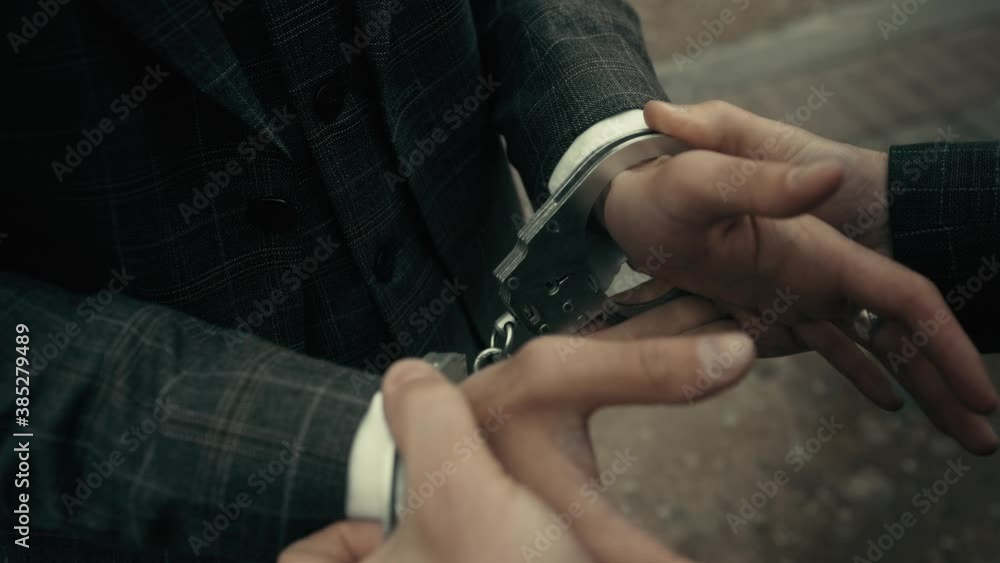 Arrest of the offender without resistance. Policeman puts the handcuffs on the hands of criminal, hands closeup. Detention of the accused business person. Arrest of the offender without resistance. Policeman puts the handcuffs on the hands of criminal, hands closeup. Detention of the accused business person.