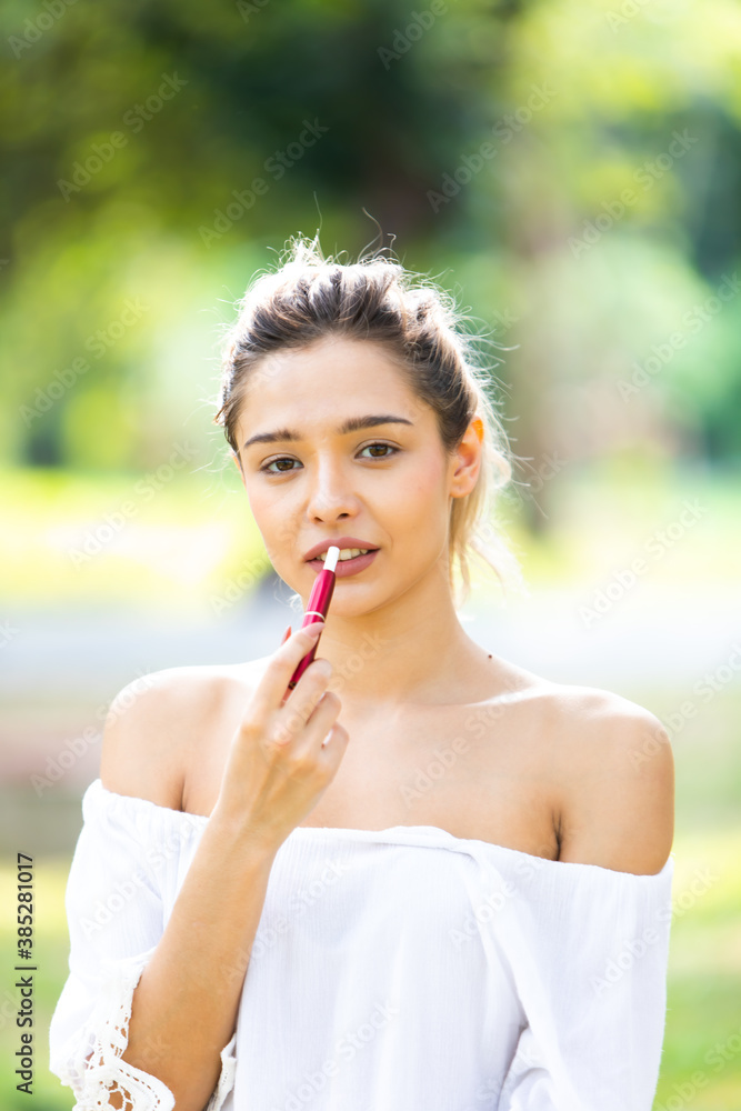 Beautiful Girl smoking electronic cigarette in green park outdoors. Caucasian woman smoking electronic cigarette Beautiful Girl smoking electronic cigarette in green park outdoors. Caucasian woman smoking electronic cigarette
