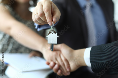 Closeup of man and woman shaking hands over keys to apartment in hands of insurance agent. Real estate sale and purchase concept.