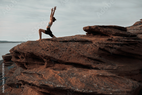 young beautiful cute blonde woman is engaged in yoga in the mountains by the sea in the light of the sun, the concept of a healthy lifestyle. gymnast stands in a warrior pose. Stretches by hands