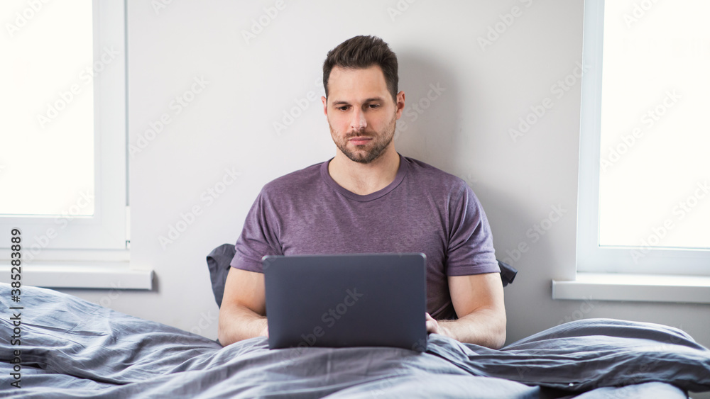 Freelancer Man Working On Laptop Online Sitting In Bed Indoor Freelancer Man Working On Laptop Online Sitting In Bed Indoor