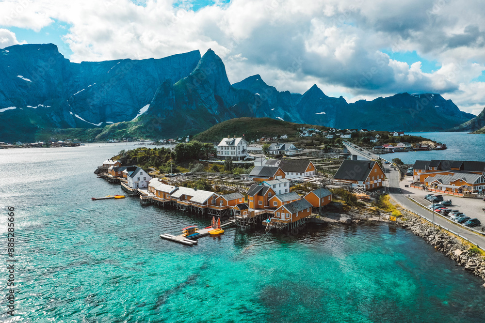 Drone view of yellow fishing cabins, mountains and turquoise ocean in Lofoten Norway