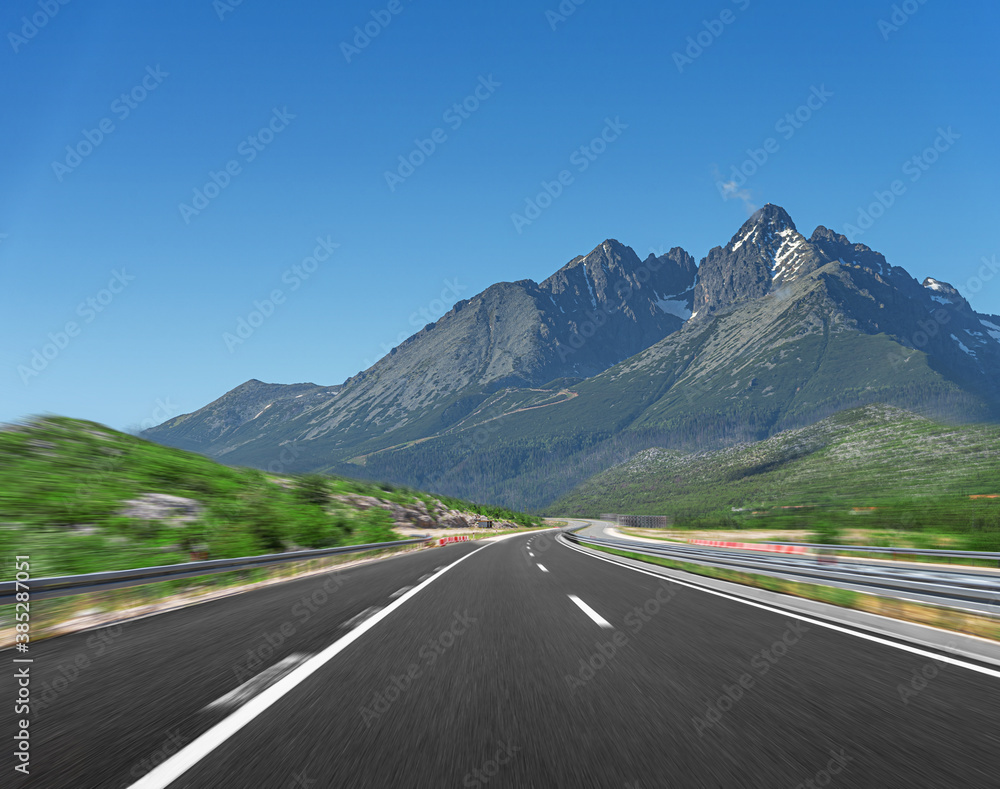 Naklejka premium big fuel gas tanker truck on highway against the backdrop of a mountain landscape.