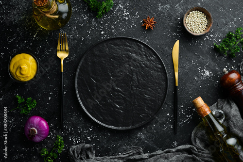 Cutlery and black plate on a black stone background. Top view. Free space for text.