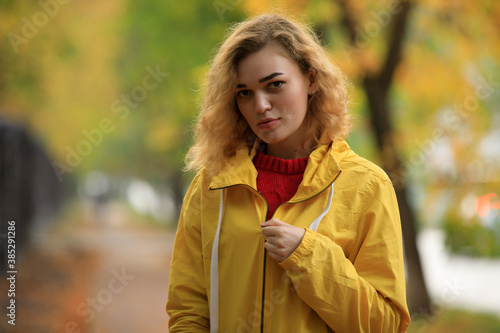 Woman in yellow jacket zips up at autumn day