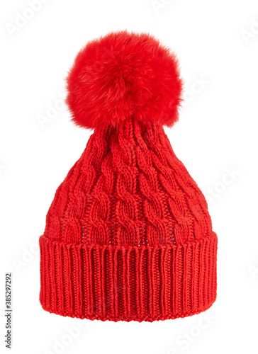 Beautiful knitted red winter cap of wool yarn with fluffy fur pompom, isolated on a white background.