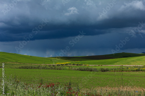 Natural beautiful landscape with stormy sky with clouds over the green field.