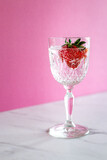 A single glass with a strawberry with bubbles on pink background and marble surface