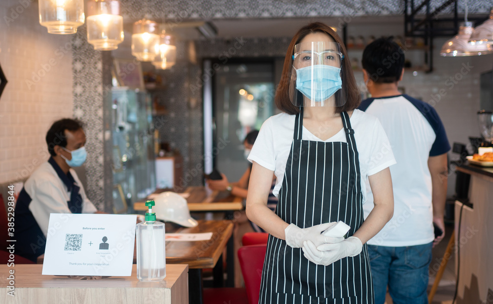Asian waitress woman wearing face masks and holding an infrared forehead thermometer to check body temperature for virus symptoms of customers before entering the restaurant ( coffee shop ). Asian waitress woman wearing face masks and holding an infrared forehead thermometer to check body temperature for virus symptoms of customers before entering the restaurant ( coffee shop ).