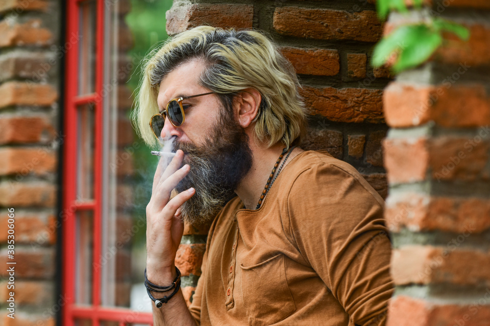 Fashionable mature man with cigarette. Brutal guy sunglasses smoking tobacco. Cool guy relaxing. Went on smoke break. Hipster smoking irish pub entrance background. Smoking outdoors. Smoking habit Fashionable mature man with cigarette. Brutal guy sunglasses smoking tobacco. Cool guy relaxing. Went on smoke break. Hipster smoking irish pub entrance background. Smoking outdoors. Smoking habit