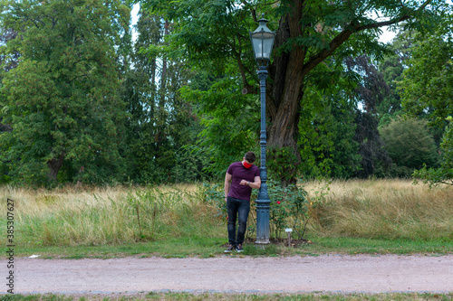 Mann mit rote Stoffmaske, wartet im Park © The-Matrixer