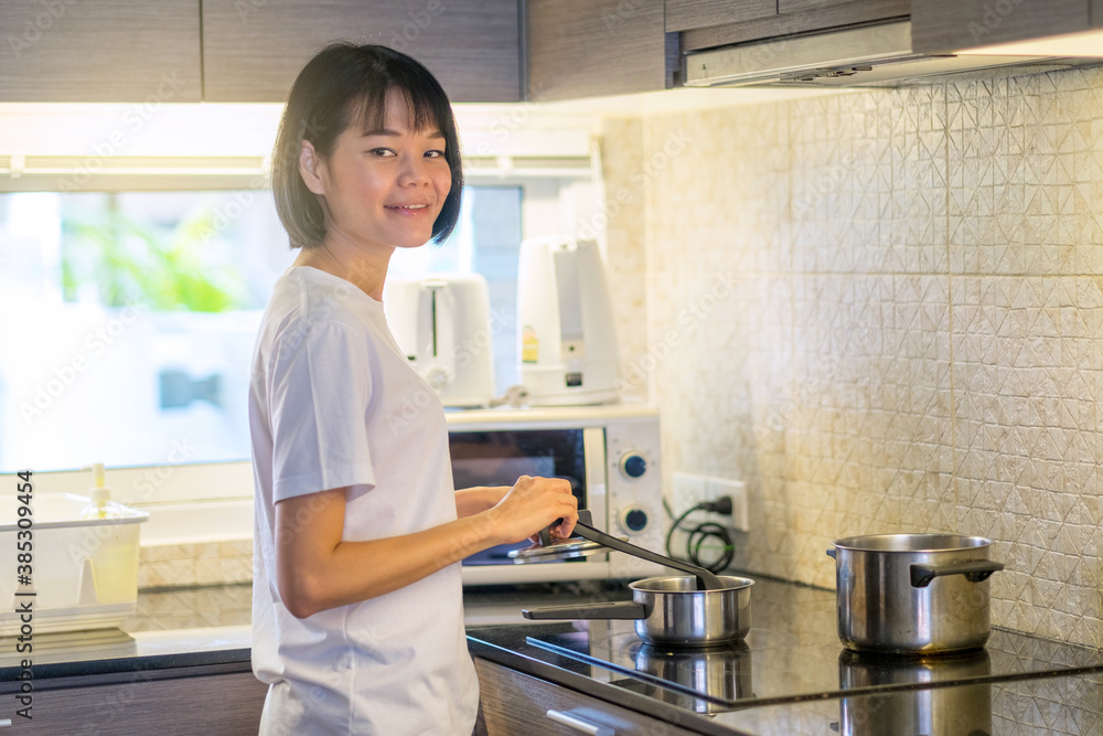             Asian woman standing by the stove in the kitchen, cooking morning breakfast food