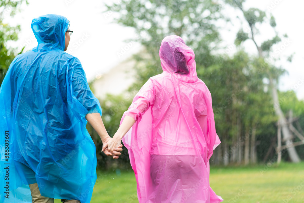 Happy Asian couple wearing a raincoat play in the rain outdoors at park.