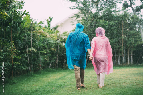 Happy Asian couple wearing a raincoat play in the rain outdoors at park.