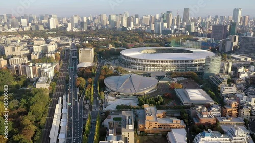 A spinning 4k drone shot of the Tokyo city area featuring two olympic venues in the foreground, the Tokyo Metropolitan Gymnasium and the Japan National Stadium and the larger Tokyo skyline.