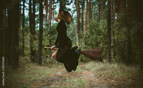 Young beautiful and mysterious Witch woman Flying on the Broom in woods. Levitation, a witch on a broom, free space. Halloween holiday, magic
