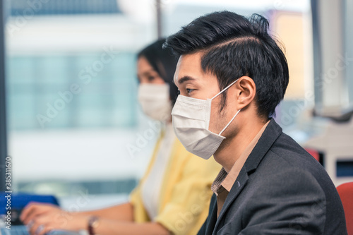 Asian male employee and woman co worker wearing face mask to protect virus infection work at office desk in company. new normal working and social distancing concept. copy space