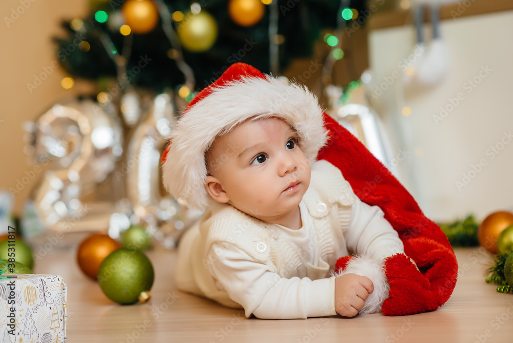 Cute smiling baby is lying under a festive Christmas tree and playing with gifts. Christmas and New Year celebrations Cute smiling baby is lying under a festive Christmas tree and playing with gifts. Christmas and New Year celebrations