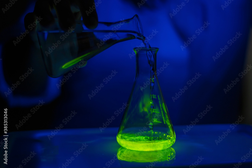 A researcher experimenting with a green fluorescent material in a glass conical flask in dark biochemistry laboratory for health care A researcher experimenting with a green fluorescent material in a glass conical flask in dark biochemistry laboratory for health care