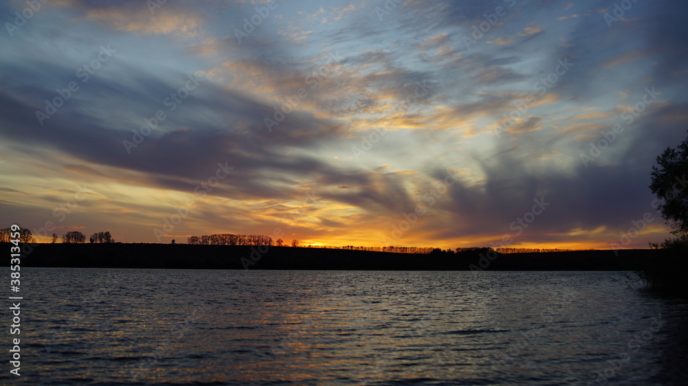 Beautiful, yellow, orange sunset with Cumulus clouds on the lake, with reflection in the water.