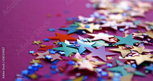 Bright glossy colorful plastic stars confetti is shining under the daylight. Pink background. Festive pattern. Close up. Flat lay.