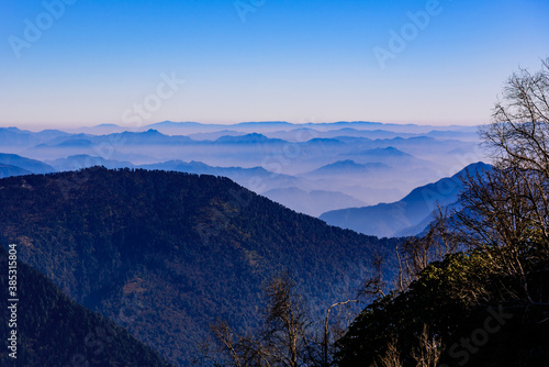 View of Himalayas mountain range with visible silhouettes through the colorful fog from Khalia top trek trail. Khalia top is at an altitude of 3500m himalayan region of Kumaon, Uttarakhand, India.
