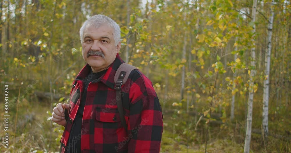 positive middle-aged hiker with backpack is smiling and looking at camera, male portrait in forest at autumn day during hiking positive middle-aged hiker with backpack is smiling and looking at camera, male portrait in forest at autumn day during hiking