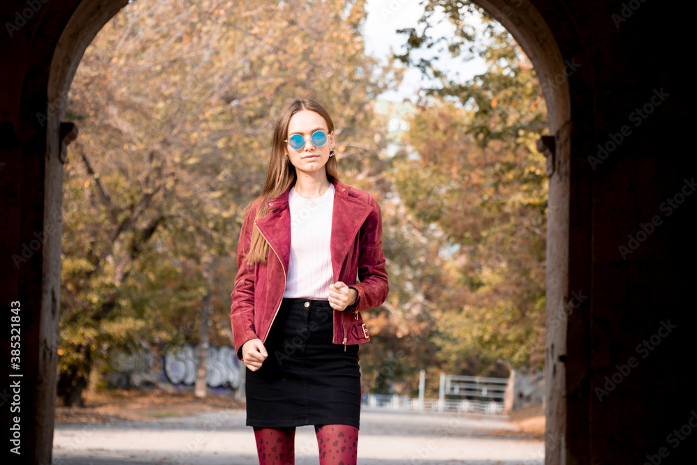 Fototapeta premium Fashionable girl in autumn clothes. Sunny day. A yellow wall made of larger bricksbehind the girl.