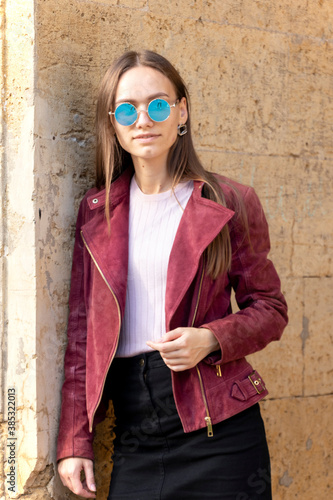 Fashionable girl in autumn clothes. Sunny day. A yellow wall made of larger bricksbehind the girl.