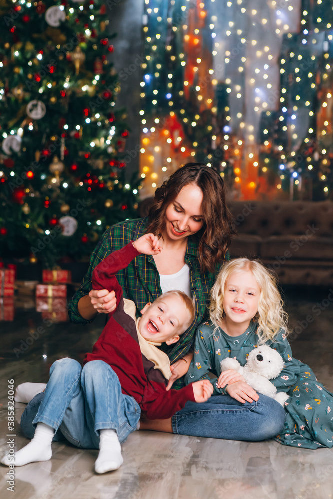 Cute mother with daughter and son posing at the Christmas tree Cute mother with daughter and son posing at the Christmas tree