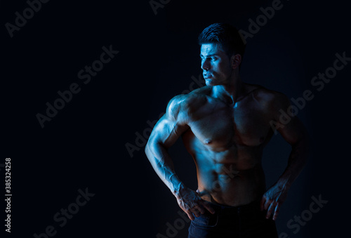 Muscular model sports young man on dark background. Fashion portrait of strong brutal guy. Sexy torso. Male flexing his muscles.