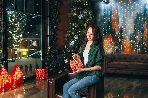 Beautiful brunette woman holds a gift box in her hands at the Christmas tree © irina_timokhina